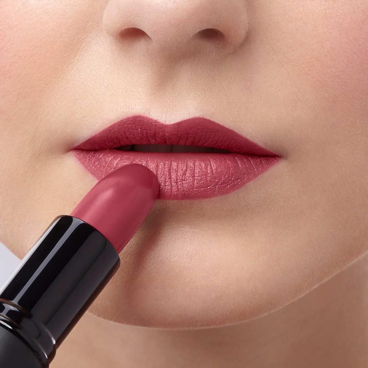 Person trägt einen rosafarbenen Lippenstift auf den Lippen auf. Der Lippenstift ist in einem schwarzen Gehäuse.