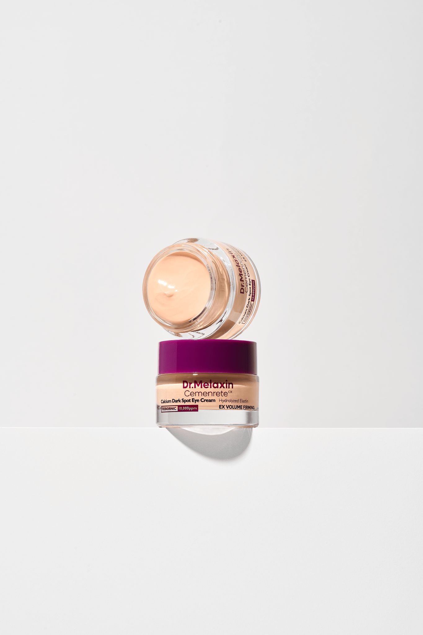 Zwei Tiegel Dr.Melaxin Cemenrete Calcium Dark Spot Eye Cream. Lila Deckel, beige Creme. Weißer Hintergrund.