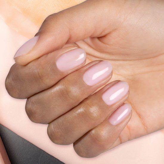 Hand mit lackierten Nägeln. Hellrosa Farbe. Abgerundete Form. Hautton. Glänzendes Finish.