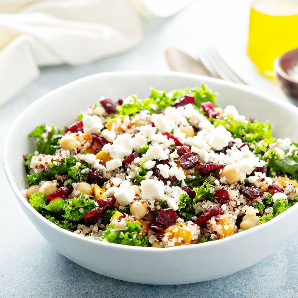 Salatschüssel mit Salat, Kichererbsen, Käse und Berberitzen. Weißer Teller, blaues Tuch im Hintergrund.