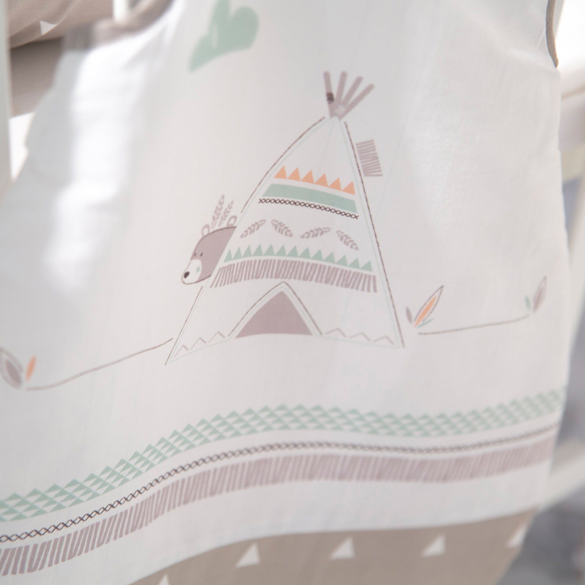 Babyschlafsack mit Bären- und Tipi-Motiv. Weiß mit braunen und grünen Akzenten. Detailansicht, teilweise im Kinderbett.