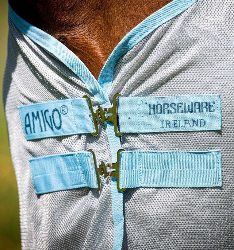 Nahaufnahme der Pferdedecke. Hellblaue Riemen mit Metallverschlüssen. Logos: AMIGO® und HORSEWARE IRELAND. Graues Netzmaterial.