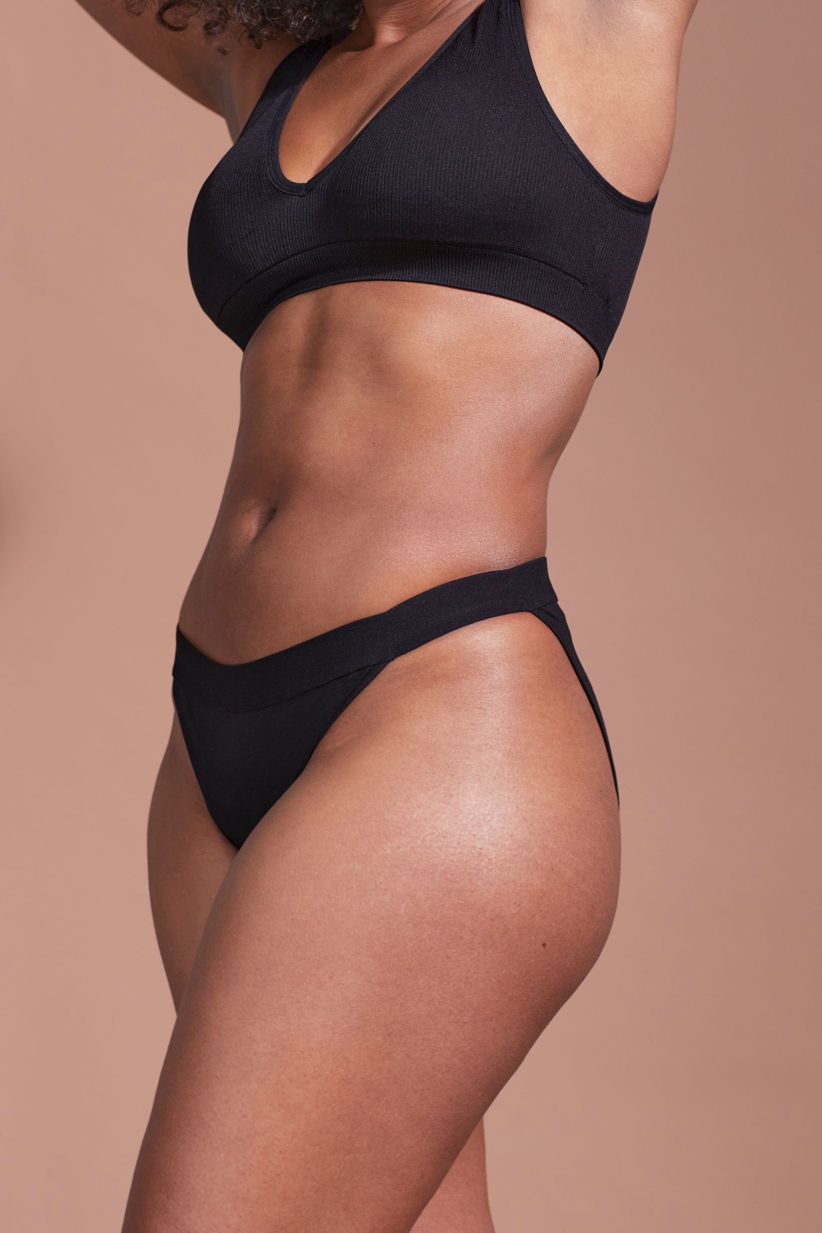 Schwarzer Slip und BH. Frau von der Seite. Gerippter Stoff.