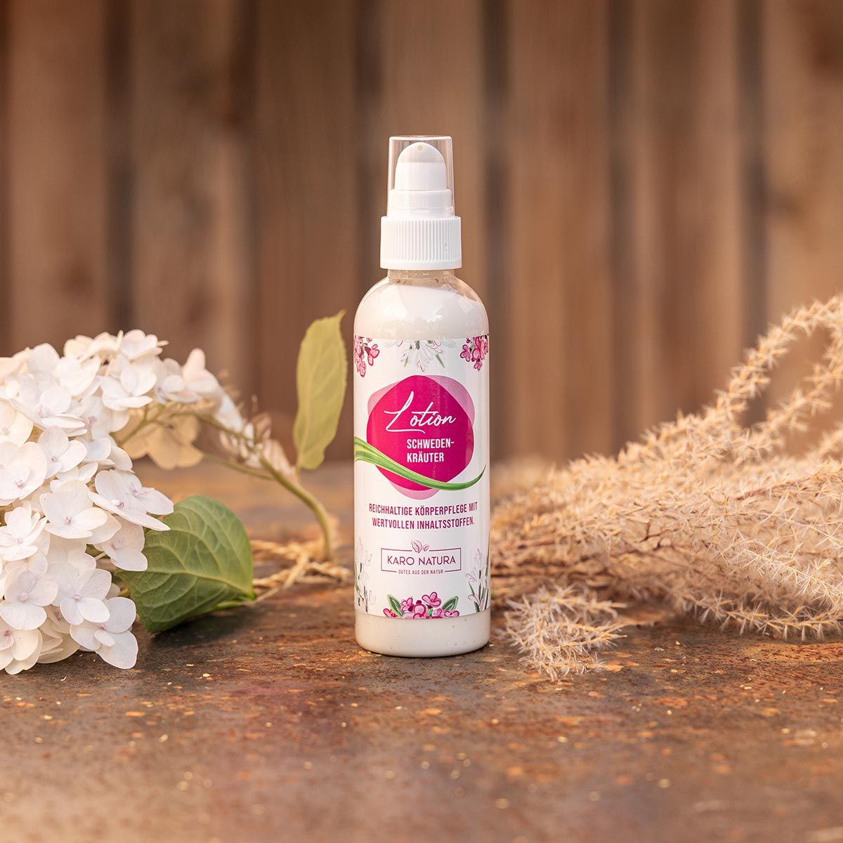 Klarer Flakon mit weißem Sprühkopf. Etikett mit 'Lotion Schwedenkräuter' und floralem Design. Karo Natura Logo. Auf Holzuntergrund.