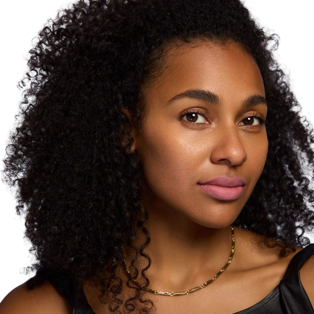 Porträt einer Frau mit Lippenstift. Goldene Halskette. Schwarzes Oberteil. Heller Hintergrund.