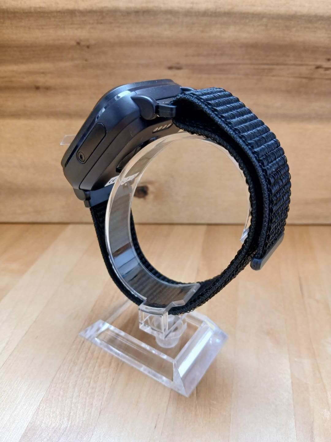 Seitenansicht einer schwarzen Smartwatch mit schwarzem Textilarmband auf einem Ständer.