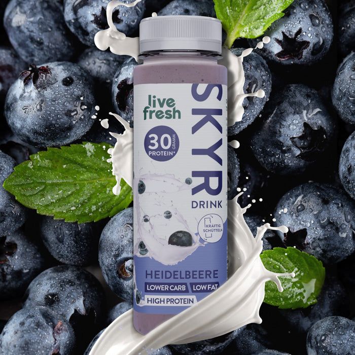 Flasche SKYR Drink mit Heidelbeer-Geschmack. Aufschrift: 30 Protein, Lower Carb, High Protein. Umgeben von Blaubeeren und Milch.