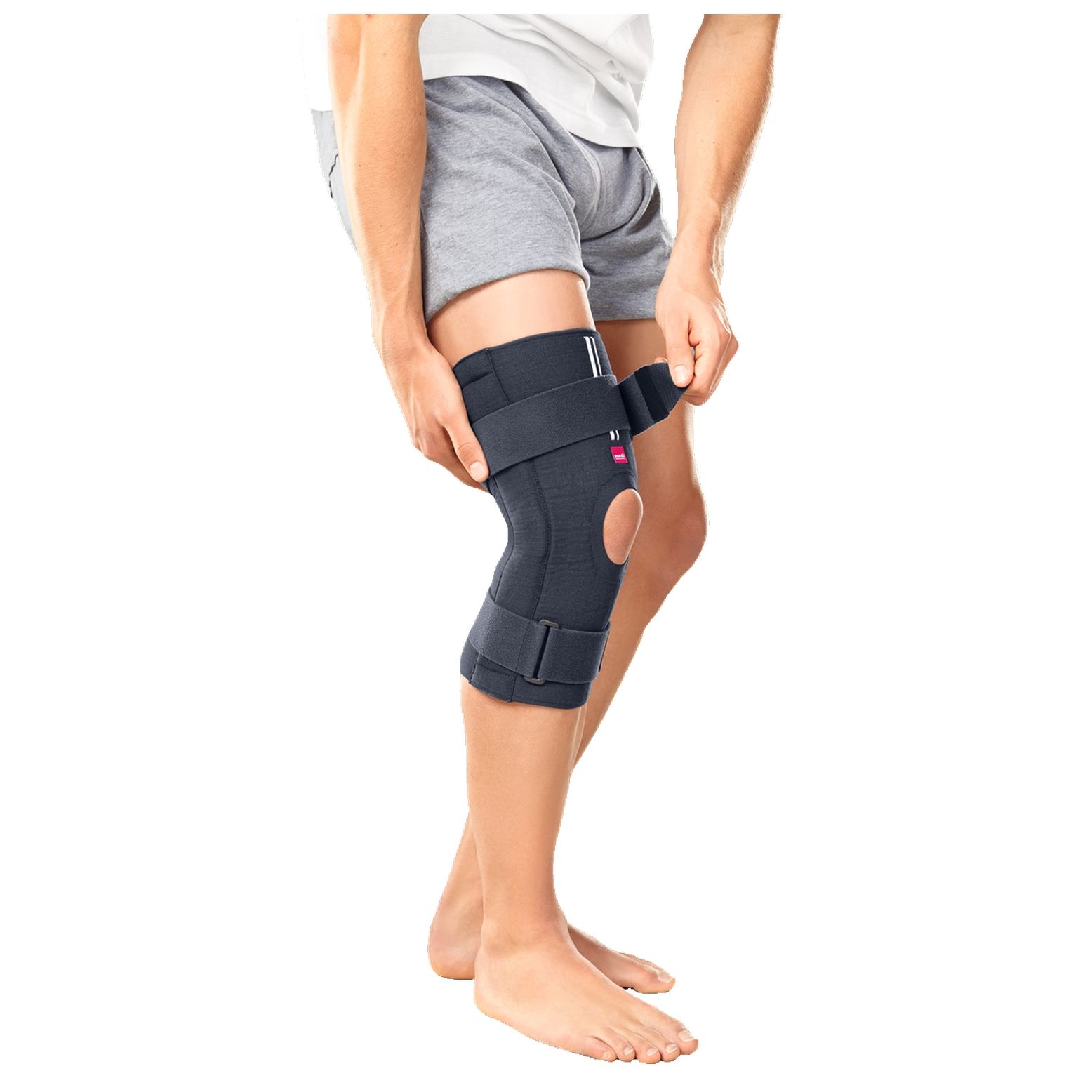 Person legt eine dunkelgraue Knieorthese an. Das Produkt hat Klettverschlüsse und eine Knieaussparung.