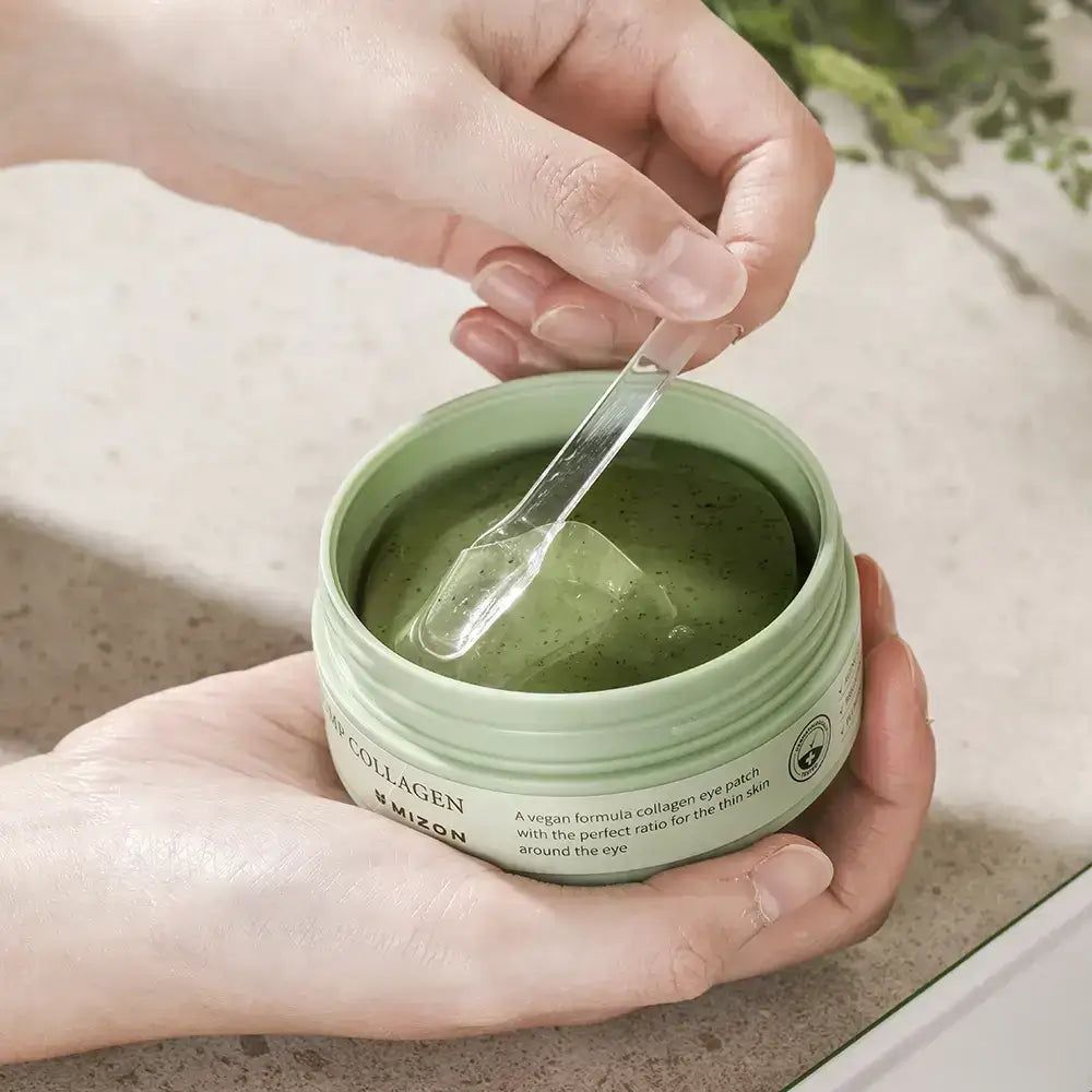 Hände mit Spatel in Dose mit Augen-Gel-Pads. Gel grün. Aufschrift: Phyto Plump Collagen Eye Gel Patch. Marke: Mizon.