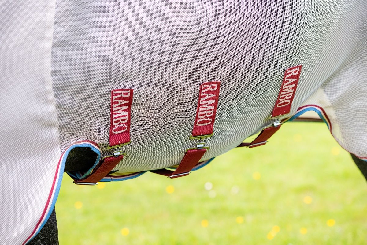 Weiße Pferdedecke mit rotem Rambo-Logo und Befestigungsgurten. Detailaufnahme.