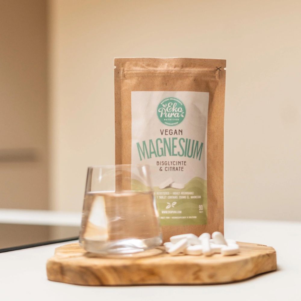Braune Verpackung mit weißem Etikett. Auf dem Etikett steht "Vegan Magnesium". Daneben ein Glas Wasser und Tabletten.