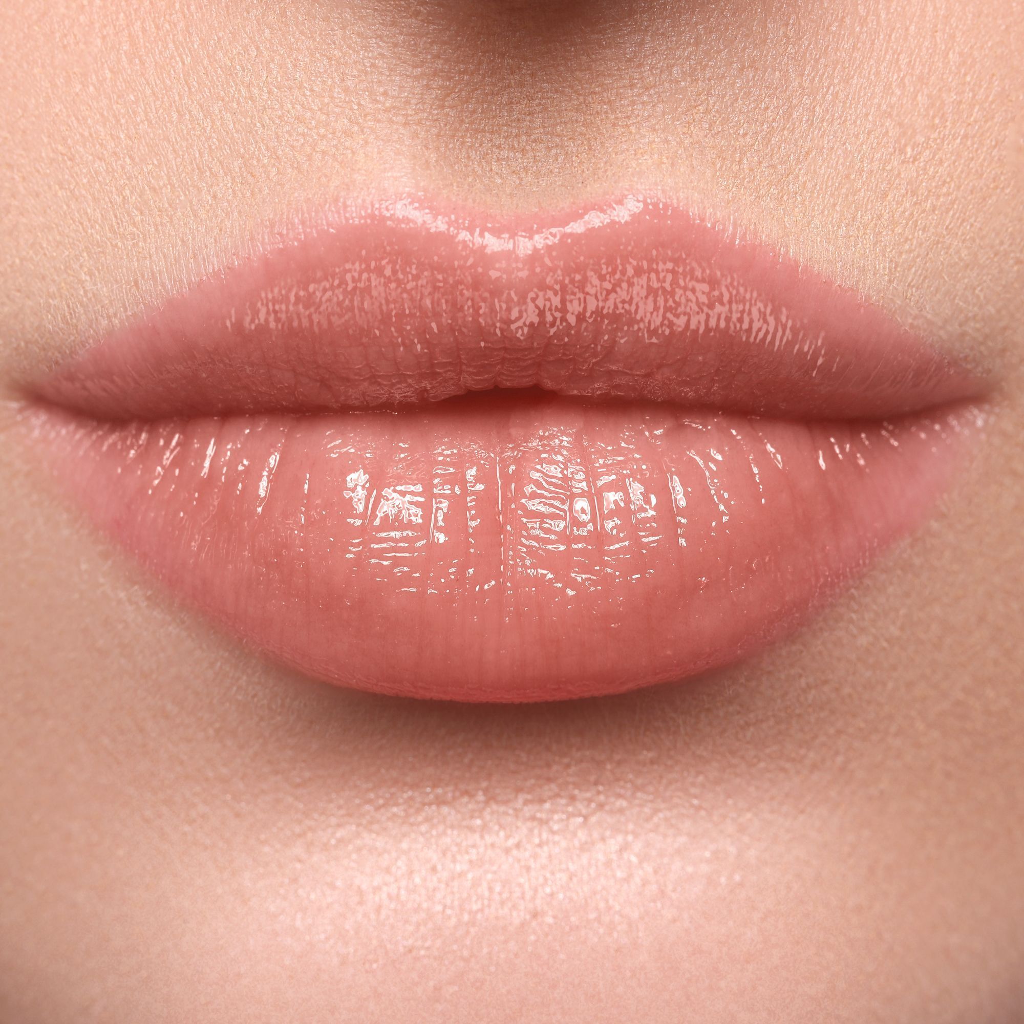Primo piano di labbra con rossetto lucido color pesca. Le labbra sono leggermente socchiuse.