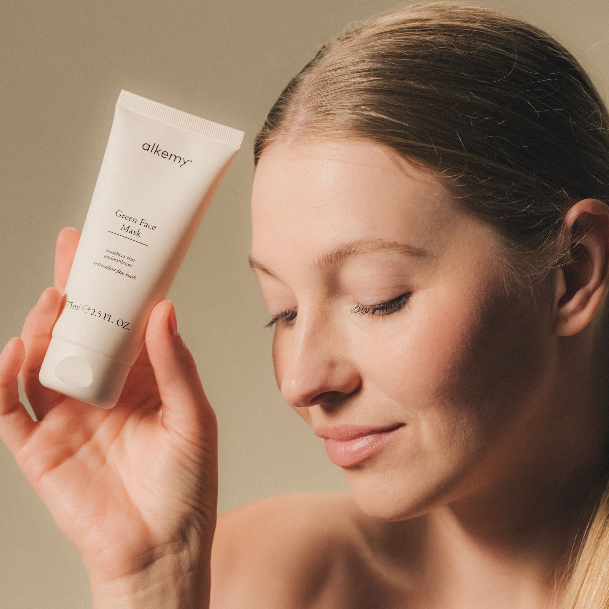 Eine Frau hält eine weiße Tube Alkemy Green Face Mask.