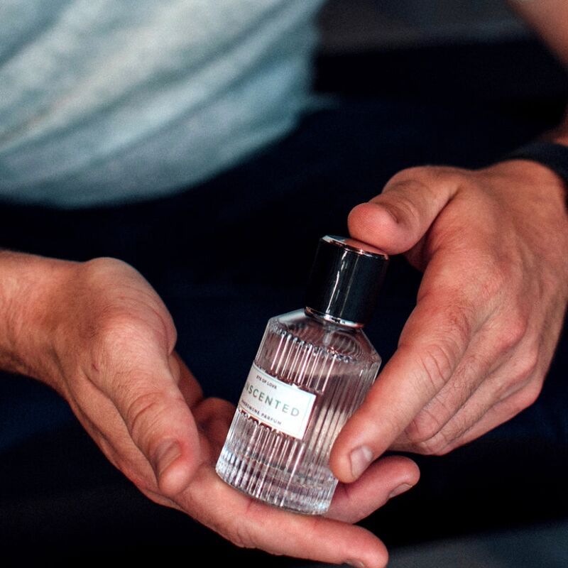 Glasflakon in Händen gehalten. Aufschrift: Unscented, Eye of Love, Pheromon Parfum. Helle Haut.
