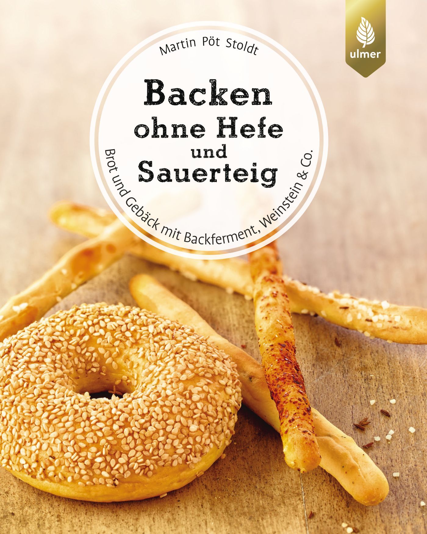 Buchcover mit Titel "Backen ohne Hefe und Sauerteig". Gezeigt werden Brotgebäck, darunter ein Sesam-Bagel und Brotstangen.
