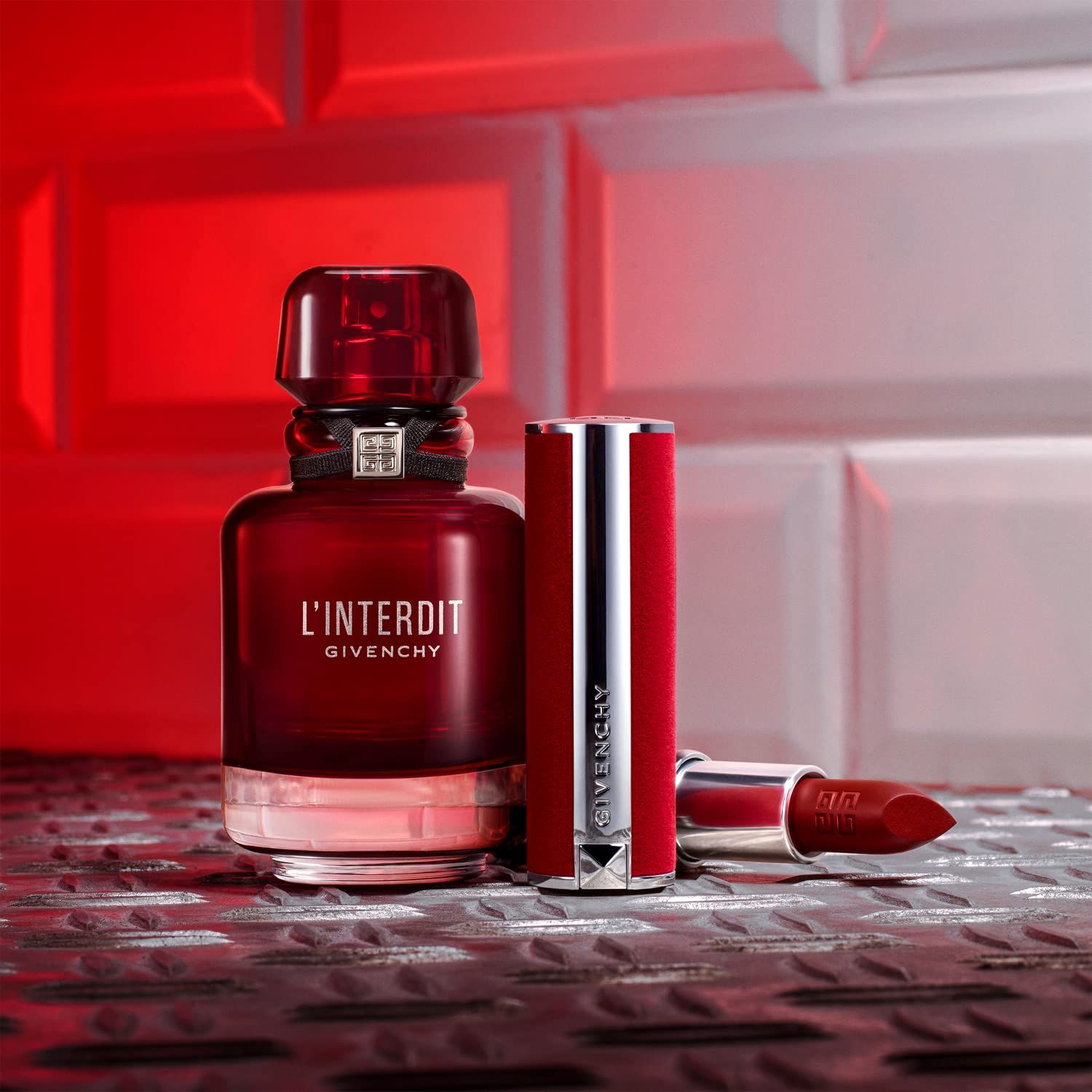 Rote Flasche mit schwarzem Band und silbernem Verschluss, daneben ein roter Lippenstift und ein geöffneter Lippenstift.
