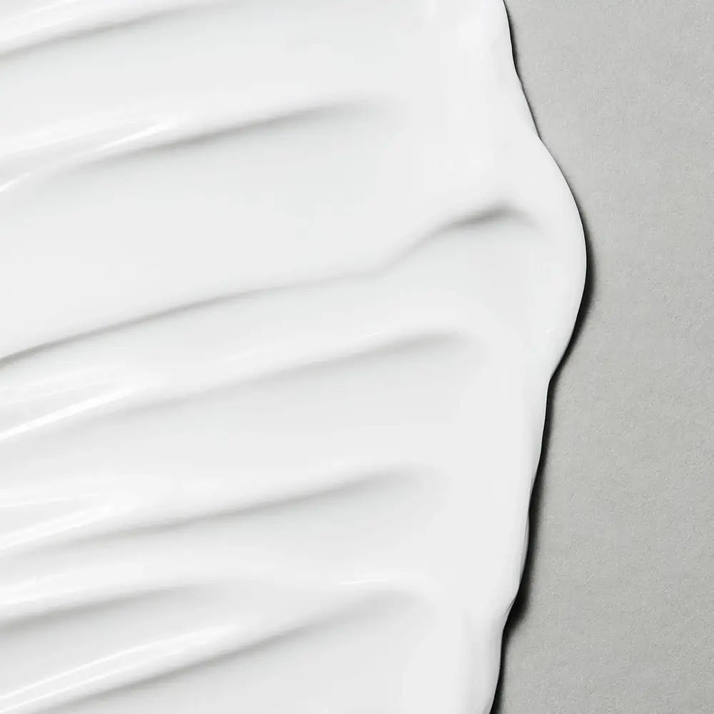 Nahaufnahme von weißer Creme. Die Creme ist glatt und hat eine wellenförmige Textur. Grauer Hintergrund.