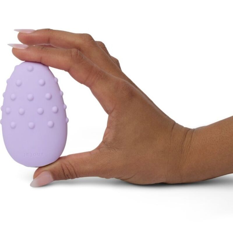 Lila Massagegerät in einer Hand gehalten. Ei-Form mit Noppen. Marke Je Joue.