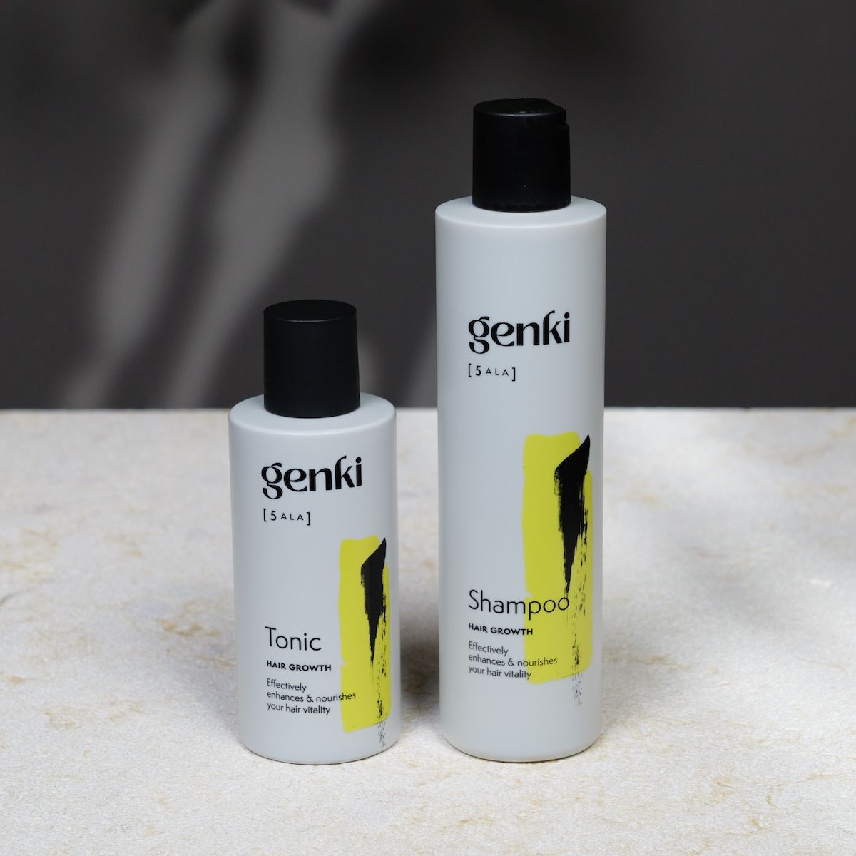 Zwei Flaschen Genki Shampoo und Tonic. Weiß, mit schwarzem Deckel und gelbem Akzent. Schriftzug: Genki, Shampoo und Tonic.