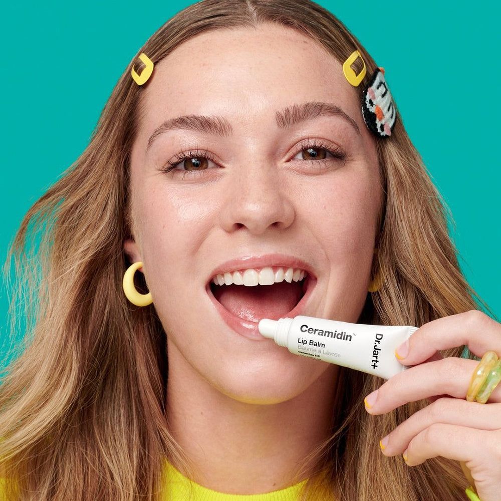 Person trägt Lip Balm auf. Gelber Hintergrund. Lippenbalsam-Tube sichtbar.