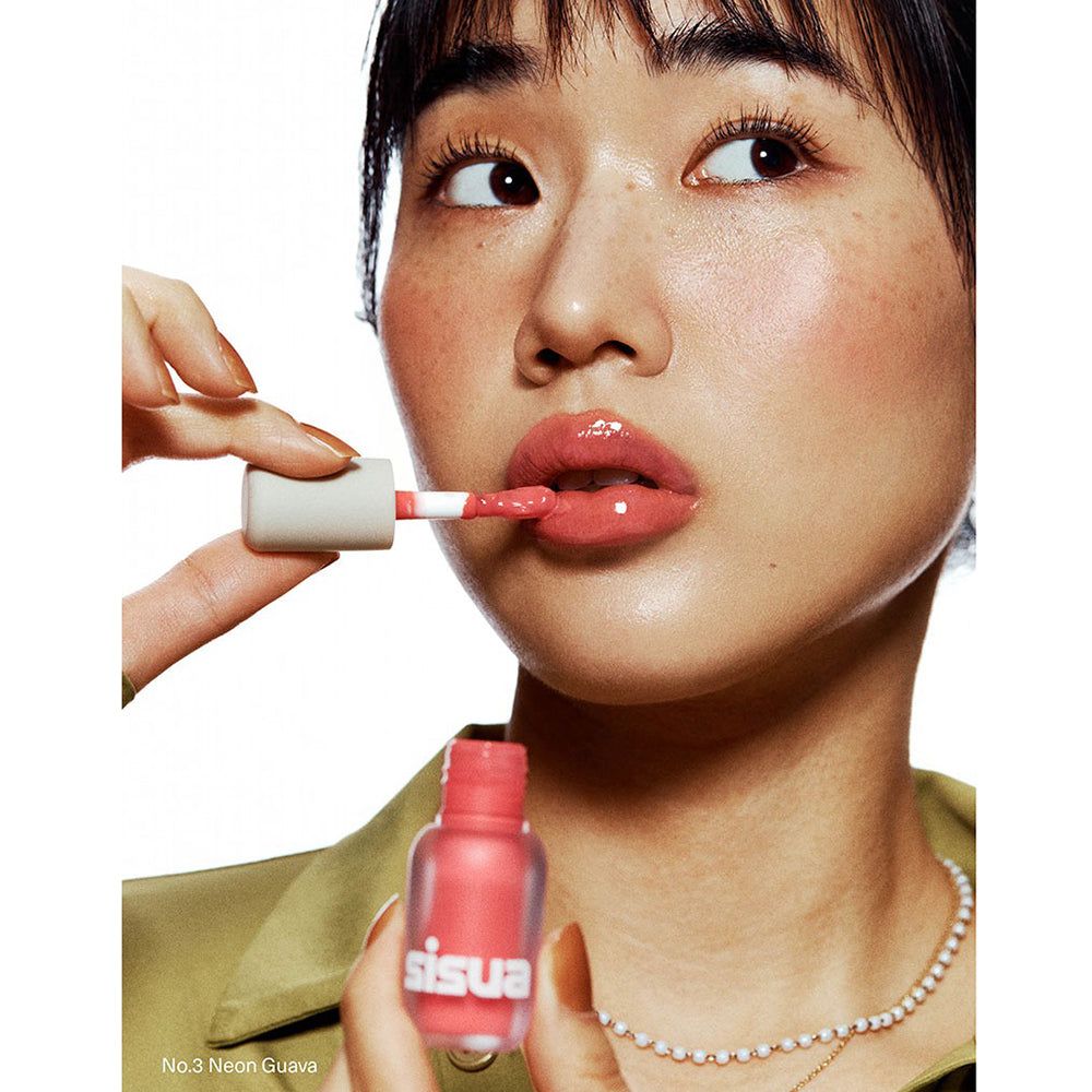 Eine Person trägt Korall-farbenen Lipgloss mit einem Applikator auf. Die Flasche ist ebenfalls Koralle.