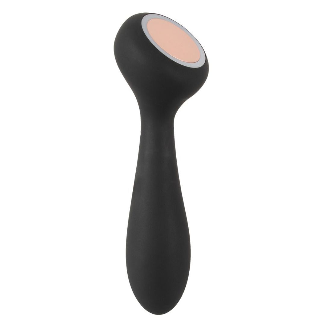 Schwarzes Wellness-Produkt mit abgerundeter Form. Oberteil mit beiger Oberfläche und silbernem Rand. Länglicher Griff.