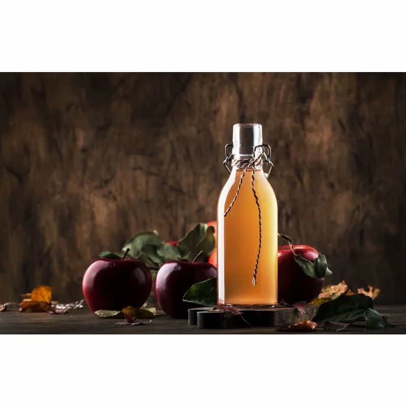 Glasflasche mit Flüssigkeit, Äpfel und Blätter. Flasche mit Bügelverschluss. Holzuntergrund.