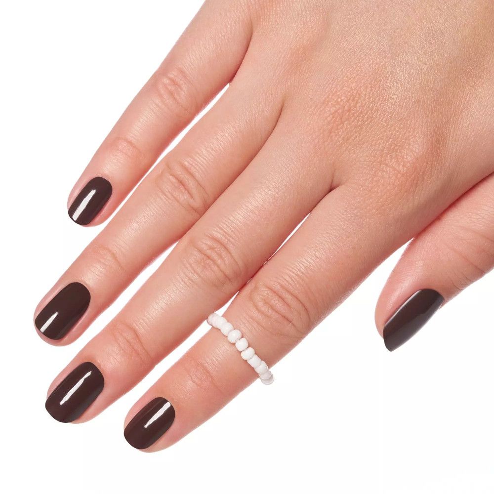 Hand mit lackierten Nägeln. Brauner Nagellack. Ring mit weißen Perlen am Finger. Weißer Hintergrund.
