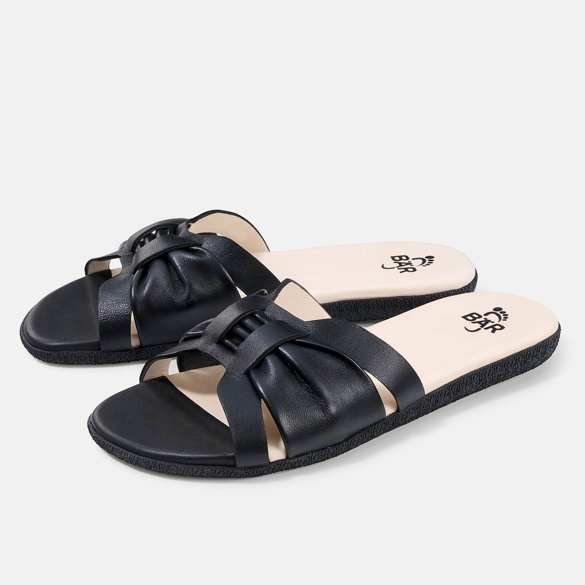 Schwarze Pantoletten mit breitem Riemen. Innensohle mit Logo. Zwei Schuhe nebeneinander.
