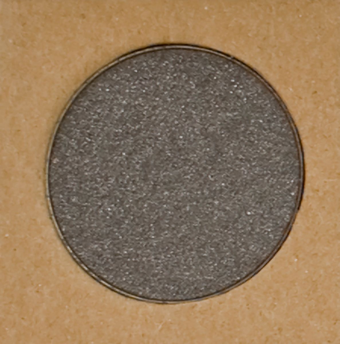Runder, grauer Lidschatten in einem braunen Behälter. Der Lidschatten hat eine glitzernde Oberfläche.