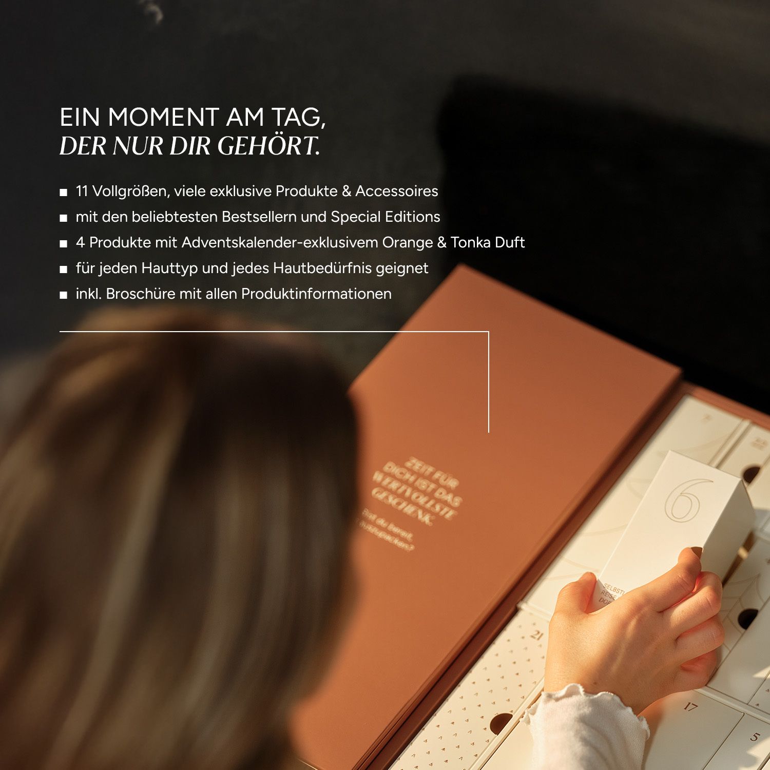 Adventskalender mit geöffneten Türchen. Braune Verpackung mit weißer Schrift. Eine Hand öffnet ein Türchen.