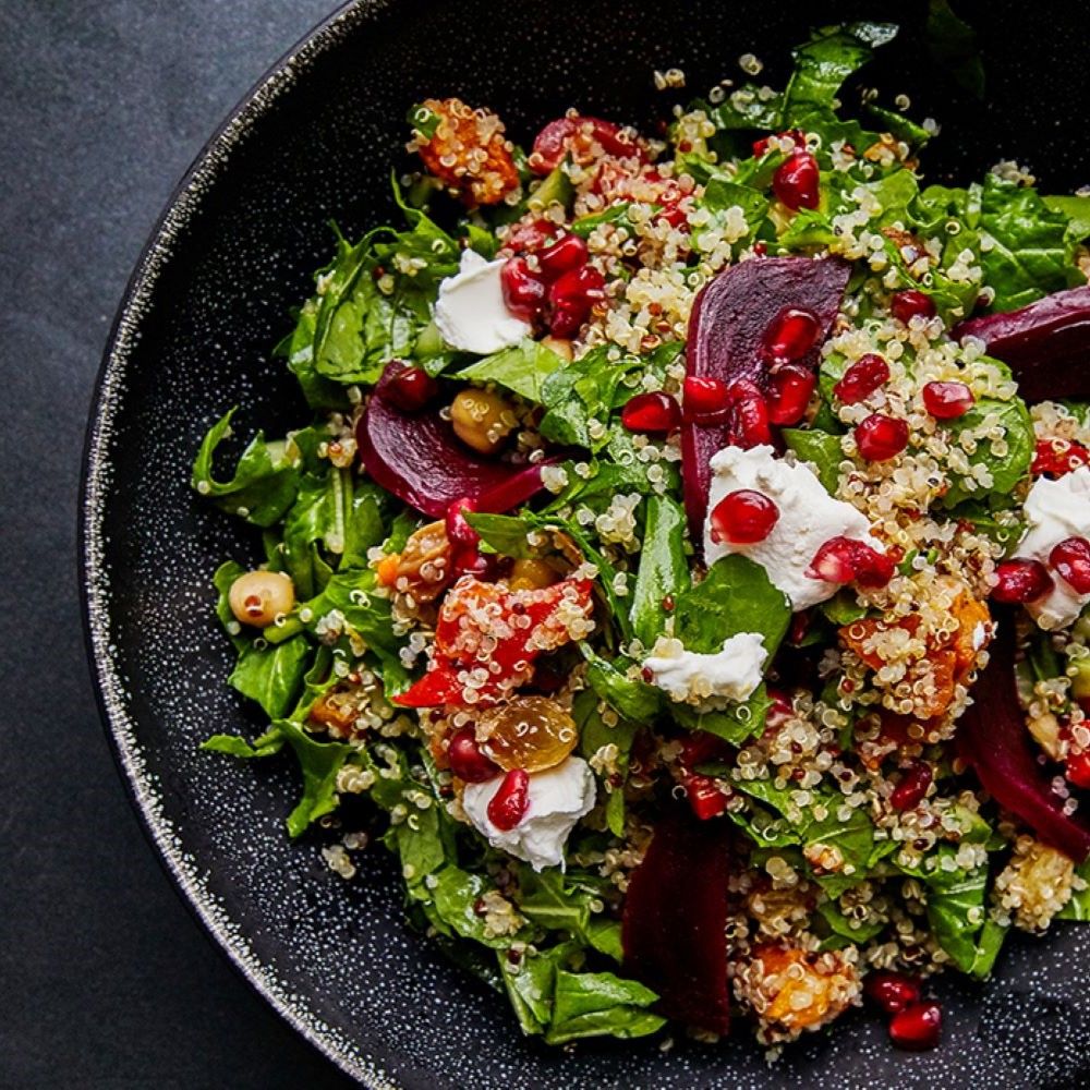 Salat in schwarzer Schüssel. Zutaten: Rucola, Quinoa, Granatapfelkerne, Rote Bete, Kichererbsen und Käse.