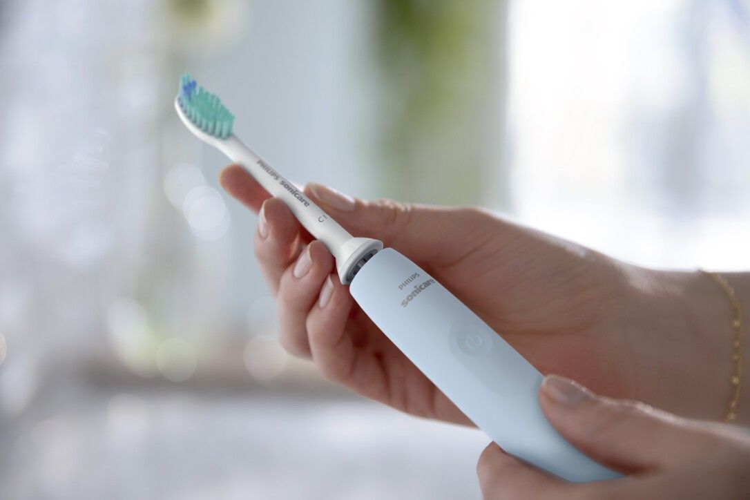 Person hält blaue elektrische Zahnbürste. Bürstenkopf mit grünen Borsten. Philips Sonicare.
