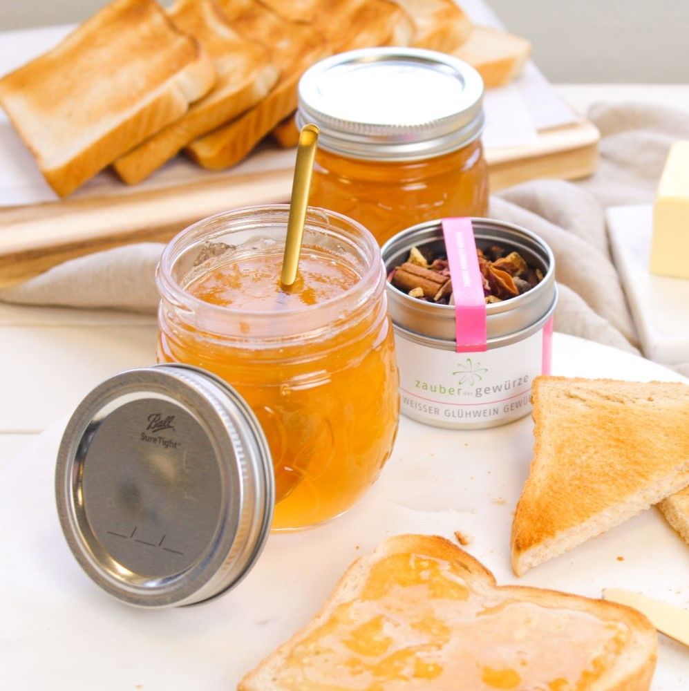Gläser mit Marmelade, Toast, Butter, und Gewürzdose mit rosa Aufkleber. Dose mit Text: Weisser Glühwein Gewürz. Goldener Löffel.