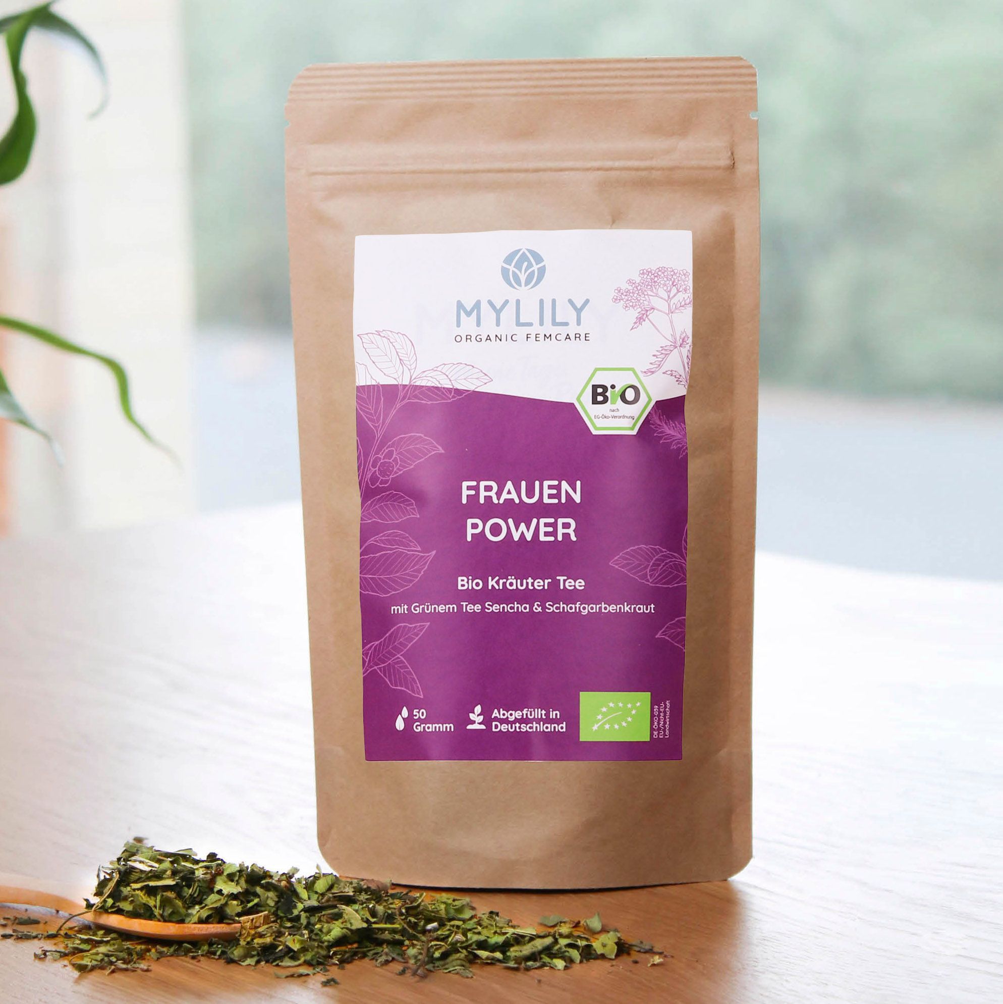 Beutel MYLILY Frauenpower Tee mit Kräutern auf einem Löffel. Braune Papierverpackung mit lila Etikett. Bio-Siegel und Text: Frauenpower.