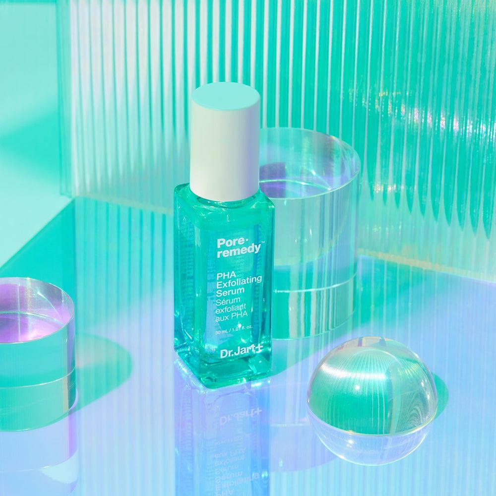 Grünes Serumfläschchen mit weißem Deckel. Aufschrift: Pore Remedy, PHA Exfoliating Serum. Auf Glasobjekten.