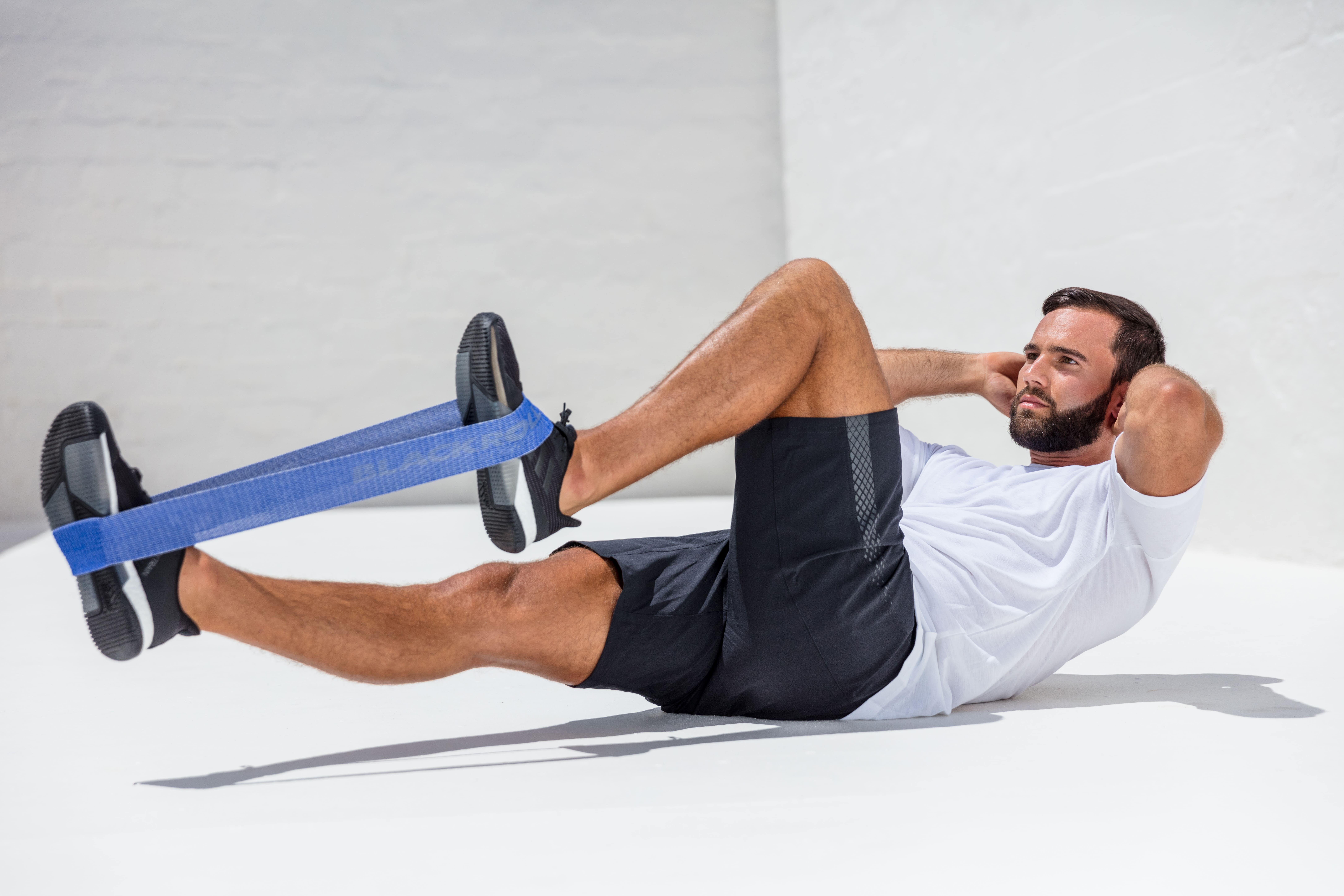 Mann trainiert mit blauer BLACKROLL Loop Band. Er liegt auf dem Rücken und macht Crunches.