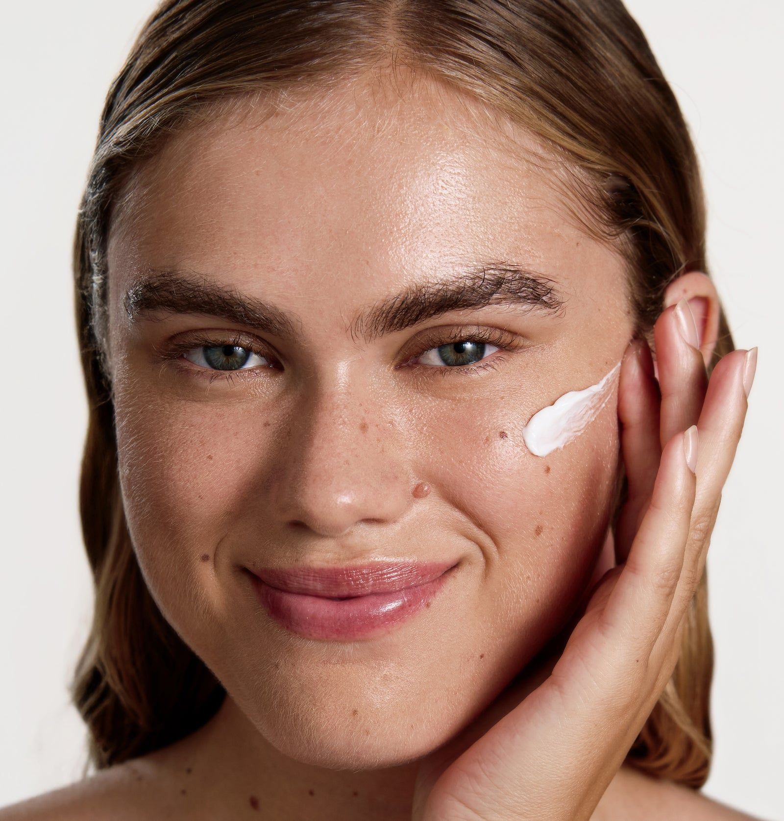 Frau mit Creme auf der Haut. Creme wird auf die Wange aufgetragen. Helle Haut, blonde Haare.