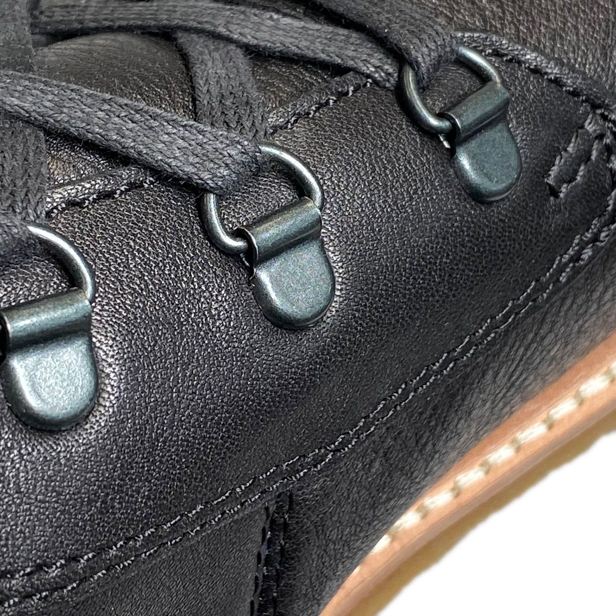Detailaufnahme der Schnürsenkelösen einer schwarzen Stiefelette. Metallösen.