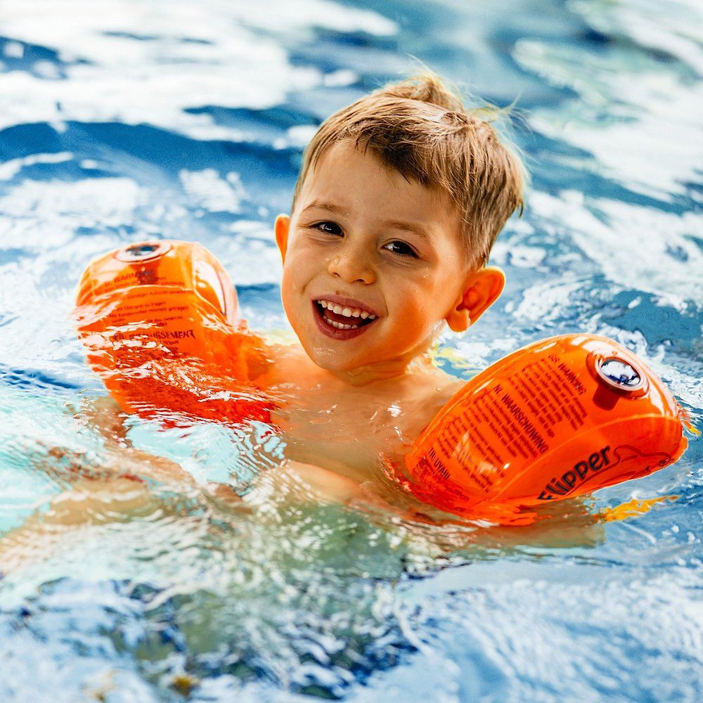 Ein lächelnder Junge trägt orangefarbene Schwimmflügel im Wasser.