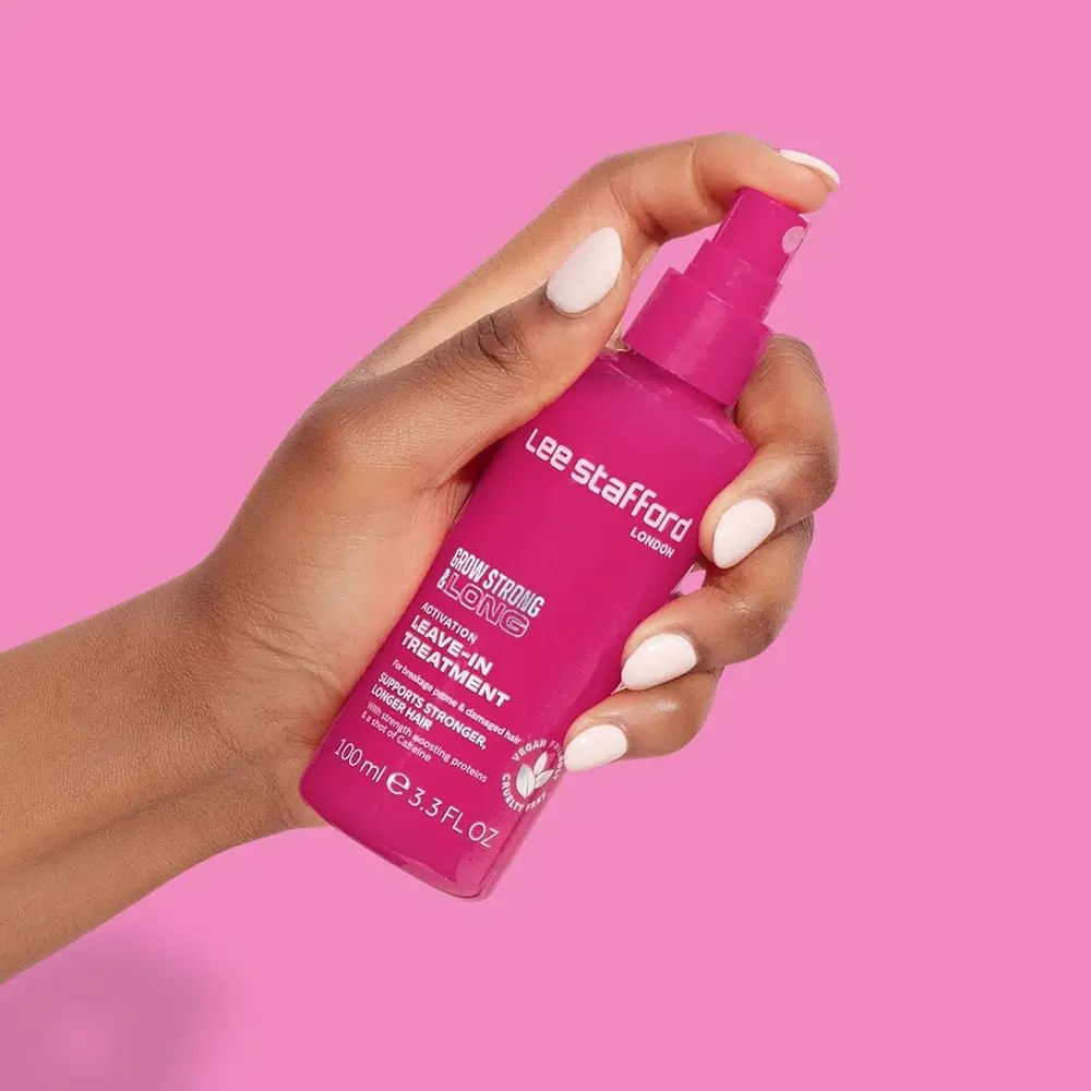 Rosa Haarspray-Flasche in einer Hand. Aufschrift: Lee Stafford, Grow Strong & Long, Leave-In Treatment. Hintergrund: Pink.