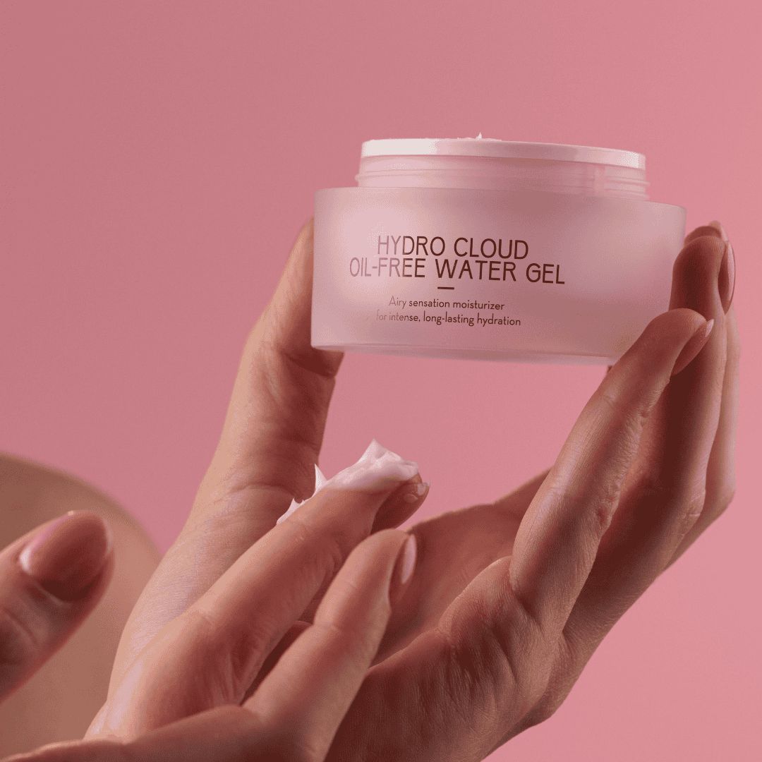 Rosa Tiegel mit weißem Deckel. Aufschrift: HYDRO CLOUD OIL-FREE WATER GEL. Text: Airy sensation moisturizer for intense, long-lasting hydration. Creme auf dem Finger.