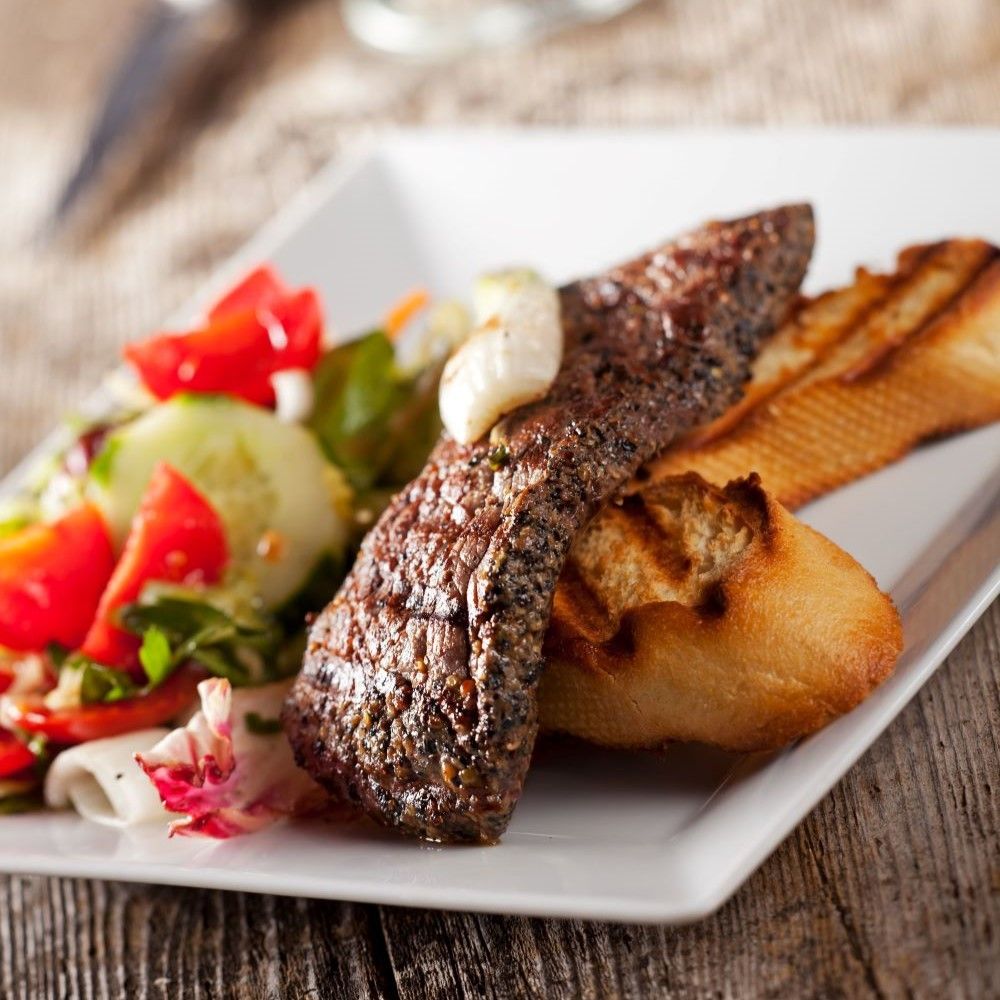 Gebratenes Steak auf einem weißen Teller mit Salat und Brot. Auf einem Holztisch.