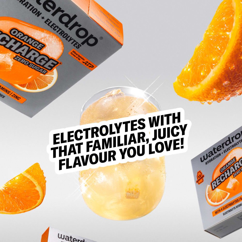 Nahaufnahme eines Glases mit orangefarbenem Getränk, umgeben von waterdrop® Orange Recharge Päckchen und Orangenspalten.