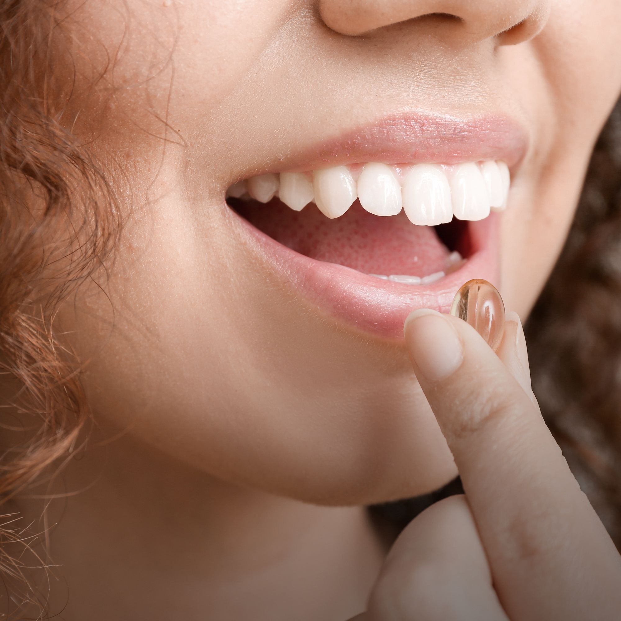 Nahaufnahme einer Person, die eine Kapsel in den Mund einführt. Sichtbar sind Zähne, Lippen und ein Finger, der die Kapsel hält.