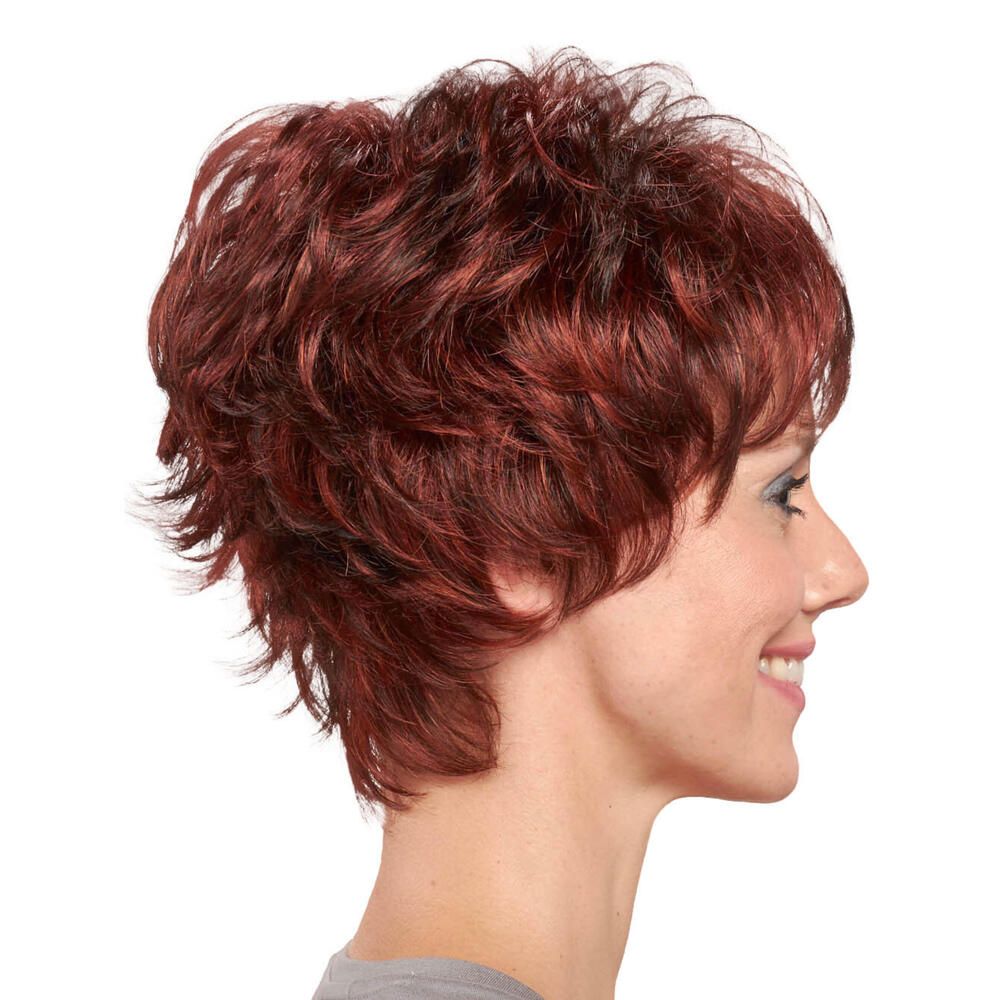 Kurzhaarperücke in Rotbraun. Profilansicht. Lockige Struktur. Pony. Frau lächelt. Graues Oberteil.
