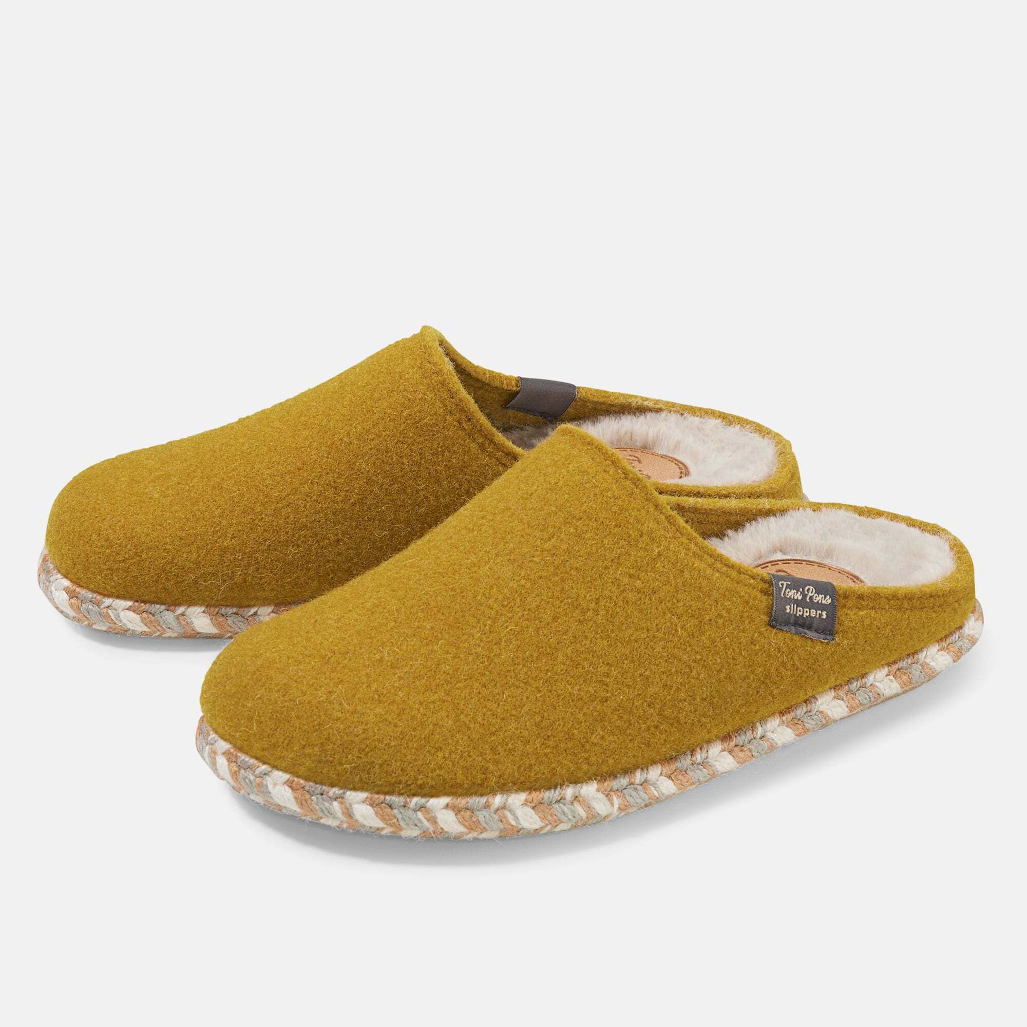 Senffarbene Hausschuhe mit weißem Innenfutter und geflochtener Sohle. Label mit Schriftzug. Zwei Schuhe nebeneinander.
