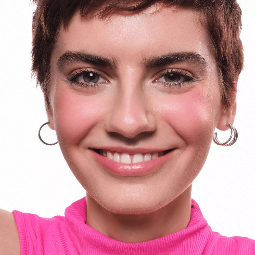 Porträt einer Frau mit rosa Rouge auf den Wangen. Sie trägt silberne Creolen und lächelt.