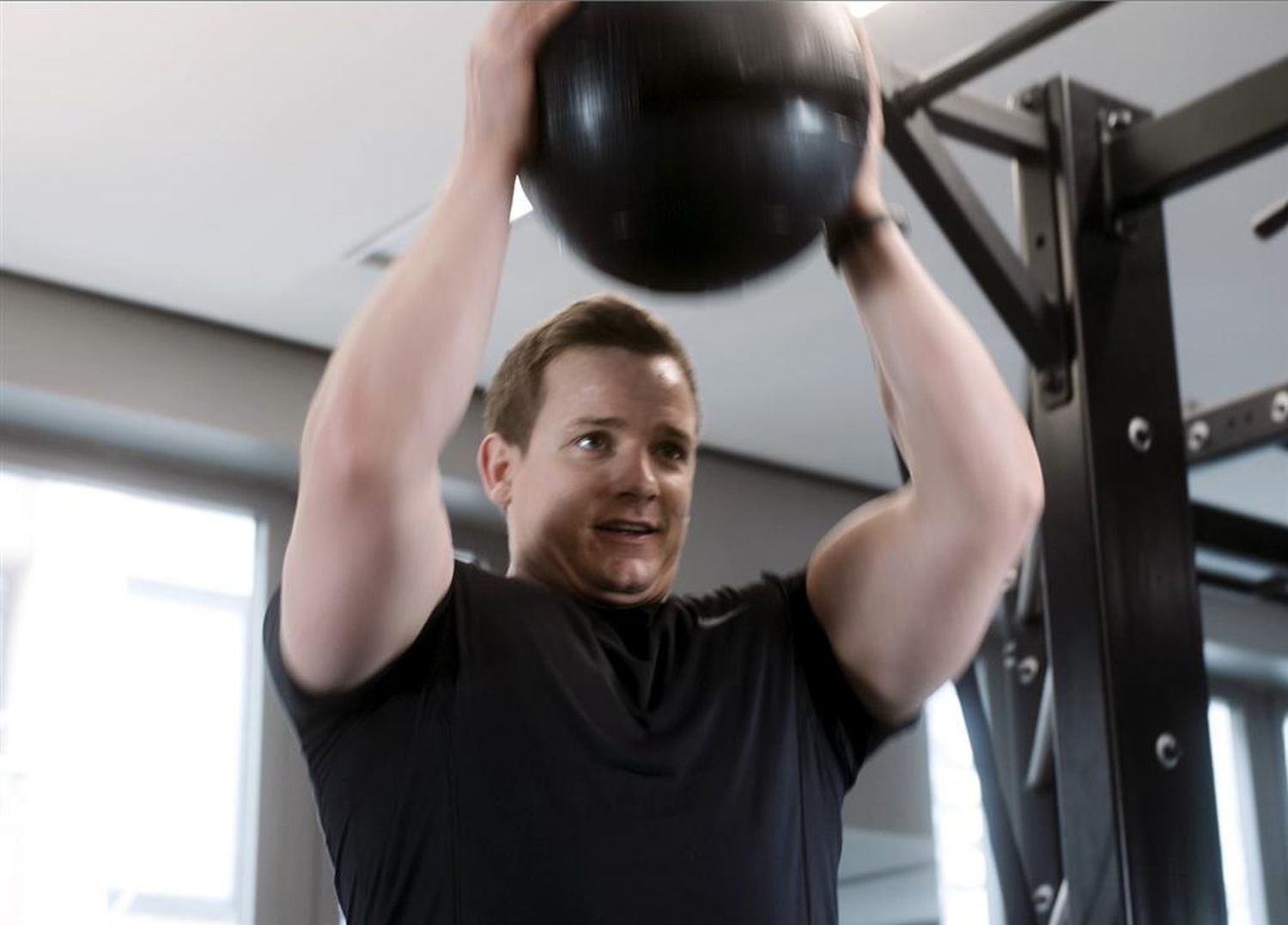 Eine Person hebt einen schwarzen Slamball über den Kopf in einem Fitnessstudio.