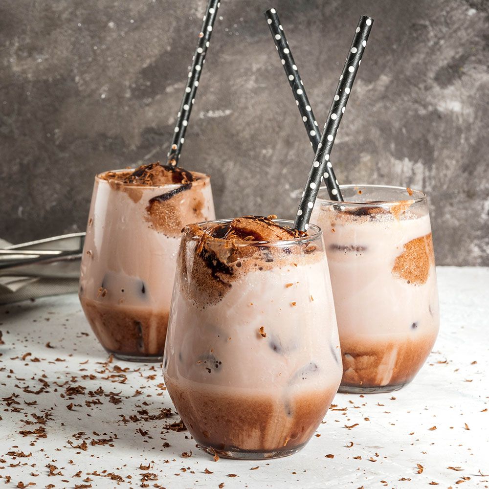 Drei Gläser mit Getränk, Eiswürfeln und Strohhalmen. Schokoladenstückchen auf der Oberfläche. Helle Flüssigkeit und Schokoladenstückchen im Glas.